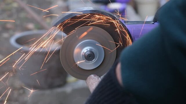 Side view close up of a man hands using a disc cutting machine to cut part of a thin metal pipe. Repair and construction work. Cordless electric tool. Metal cutting.