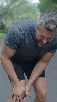 Knee joint dislocation after running. Sport injury. Arthritis. Man massage knee at pain point. Running injury outdoor. Knee pain during workout. Painful trauma. Man runner has knee pain. 4k vertical