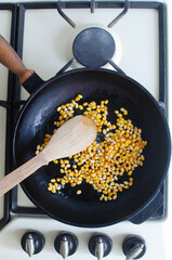 Kernels in oil are heated in a black frying pan