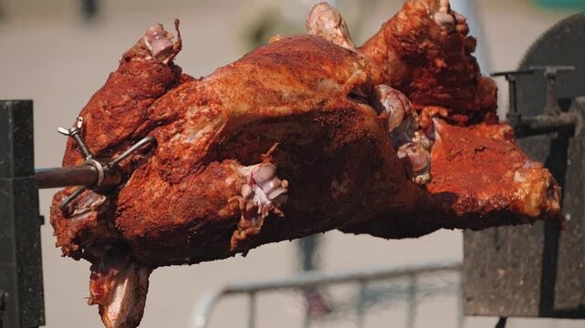 A whole roasted pig on a spit, showcasing a crispy, well-seasoned exterior. The meat is expertly cooked, revealing its rich texture and appetizing appearance against a blurred background