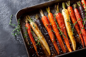 Oven roasted carrots with fresh thyme and sea salt on an enamel tray. Simple rustic vegetable side dish with warm natural colors.