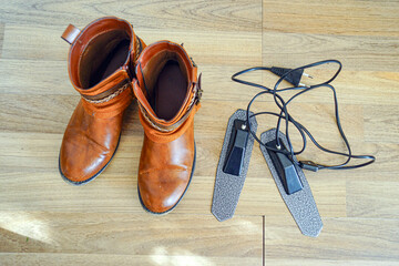 Pair of women's low boots made of eco-leather positioned beside electric warming inserts for effective moisture removal. Represents rainy season essentials and footwear drying solutions.