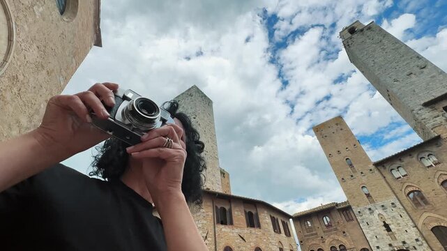 Happy smiling woman photographer with vintage camera taking photos of historic towers in San Gimignano, Tuscany in an urban setting