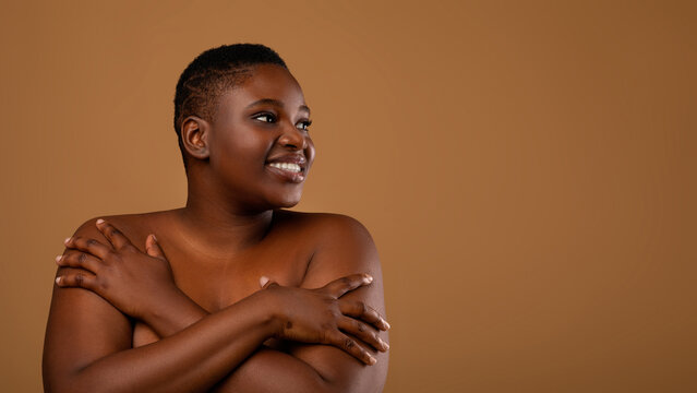 Beauty Care. Portrait Of Young Smiling Nude Black Woman With Perfect Skin Hugging Herself Embracing Bare Shoulders Posing Isolated Over Brown Background, Looking Aside At Free Copy Space, Panorama