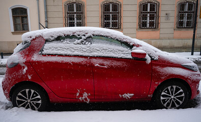Romania, Cluj-Napoca  1/07/2026: Snow covered red car parked on a city street during winter