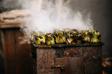 Fresh Artichokes Barbecue At Catania Market In Sicily: Trimming And Steaming Green Vegetables On Hot Surface In Traditional Street Food Scene