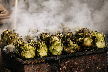 Fresh Artichokes Barbecue At Catania Market In Sicily: Trimming And Steaming Green Vegetables On Hot Surface In Traditional Street Food Scene