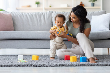 Caring Black Mom And Her Adorable Infant Son Playing With Toys At Home, Young African American...