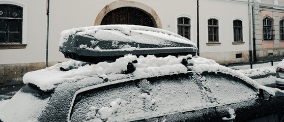 Snow covered car with roof box parked on city street in winter