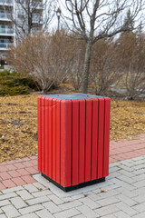 Red wooden trash bin on brick walkway in park. Garbage can on sidewalk.