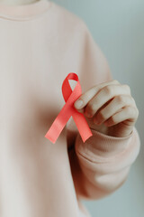 Individual holding a red awareness ribbon in a soft pink sweater, symbolizing support for health causes, with a neutral background emphasizing the message of awareness and solidarity