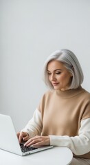 Mature woman with silver hair working on a laptop. Vertical portrait of a professional senior woman typing at a desk. Digital literacy and remote work concept