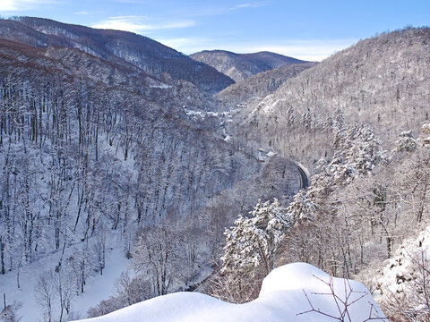 Winter panorama from Moln&aacute;r Rock featuring a wooden cross and a snow-covered forested valley overlooking the village of Als&oacute;h&aacute;mor in the B&uuml;kk Mountains, Hungary.