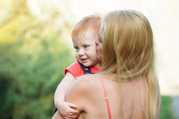 Mom and son outdoors in the summer. Mother is holding the kid boy in her arms and kissing him