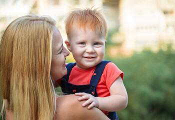 Mom and son outdoors in the summer. Mother is holding the kid boy in her arms and smiling him