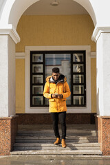 African american man standing near building entrance using smartphone in sunlight. Technology, communication, and urban lifestyle in modern architecture environment.