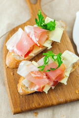 Gourmet sandwich with prosciutto and cheese on wooden board