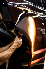 Process of paintless dent repair on car body. The mechanic at the auto shop with tools to repair dents in car body. Body repair. A specialist repairs a dent on the car body without painting. PDR. 