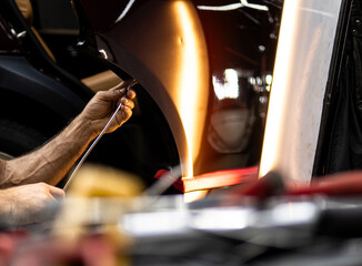 Process of paintless dent repair on car body. The mechanic at the auto shop with tools to repair dents in car body. Body repair. A specialist repairs a dent on the car body without painting. PDR. 