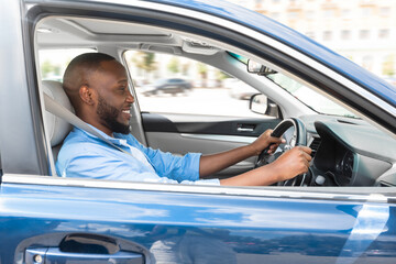 Happy Driver. Side view profile portrait of cheerful positive African American man sitting in a car on driver's seat. Excited black guy riding in the city, holding hands on steering wheel © Prostock-studio