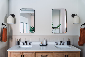 Fototapeta premium Modern double sink bathroom interior with minimalist design, white walls, wood vanity, matte black fixtures, rectangular mirrors, wall sconces, natural light, neutral tones, contemporary home decor