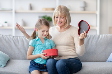 Excited woman open birthday present together with granddaughter, spending time at home having fun,...