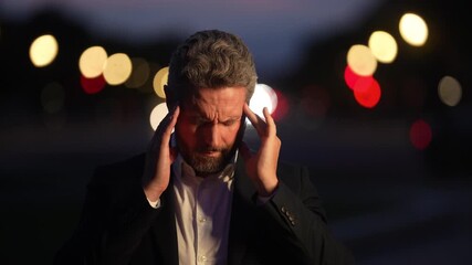 Man experiencing burnout after long workday. Mental health awareness concept with man. Businessman worried and exhausted at night. Stressful urban life portrait.