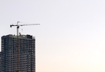 Tower crane towers over high-rise under construction at golden hour, symbolizing urban growth.