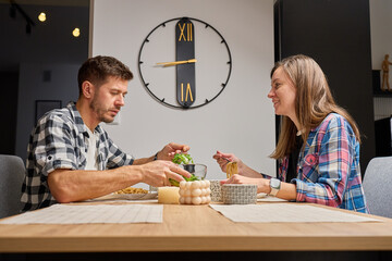 Man and woman sitting at dining table and eating pasta and salad