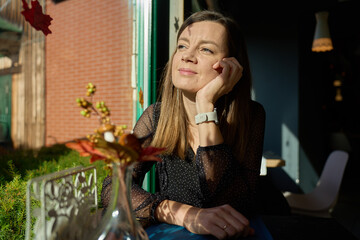 Woman sitting by window in cafe looking into sunlight