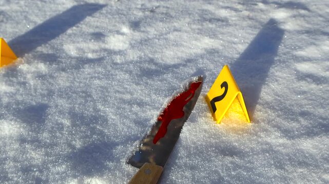 Close up pullback of a bloodied knife in sunlit snow revealing forensic markers and red splatter, forming a dramatic winter crime scene with shallow depth and long shadows.