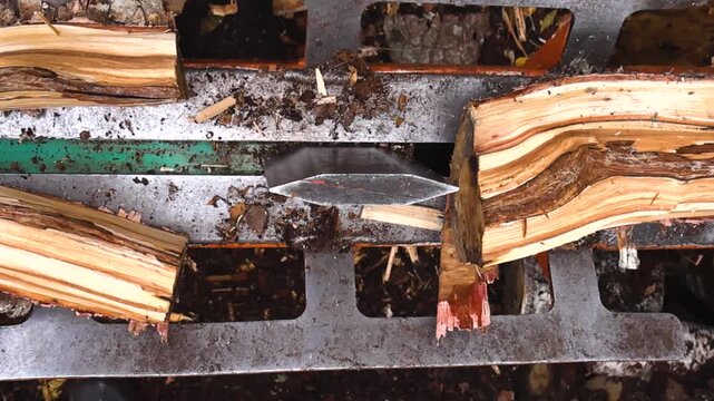 Top down view of a mechanical log splitter cutting a pine firewood piece in half, with flying bark fragments, wood dust, and detailed natural textures in an outdoor setting.