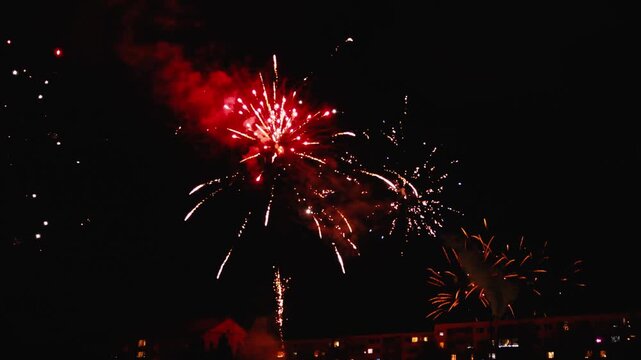 Vibrant New Year&rsquo;s Eve fireworks exploding above city apartment buildings at night, creating colorful bursts, glowing smoke, and a festive urban atmosphere.