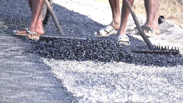 Workers laying asphalt on street road. Indian road construction by indian labors. Road construction with hot mix asphalt. Bitumen surfacing on rural road.
