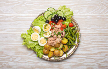 Nicoise salad with tuna, eggs, potatoes, green beans, and olives on a white table