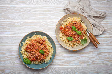 Two plates of spaghetti bolognese with basil on wooden table