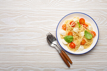 Plate of spaghetti pasta with cherry tomatoes and mozzarella cheese on white wooden background with