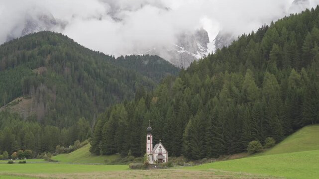 Chiesetta di San Giovanni in Ranui in Val di Funes, Italy, standing before misty Geisler peaks in South Tyrol. An atmospheric alpine landscape ideal for travel tourism and religion concepts.