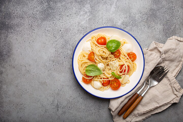 Spaghetti with cherry tomatoes and mozzarella being served on a plate with copy space