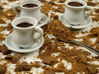 White cups with hot chocolate and a teaspoon with cocoa powder, top view, pieces of milk chocolate on a white background, side view 