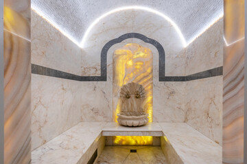 A stunning spa room features a marble fountain at its center, surrounded by soft yellow lighting....