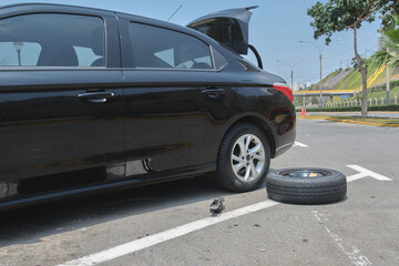 Black sedan experiencing a breakdown with a spare tire and car jack on the asphalt
