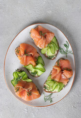 Sandwiches with salted salmon, cream cheese and cucumber on white plate, Top view