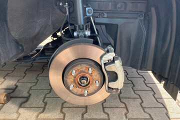 Vehicle disc brake assembly with removed wheel metal brake rotor and caliper are visible on a car hub.