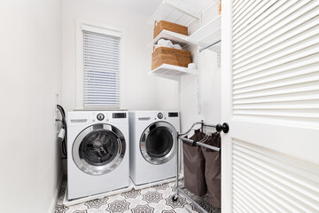 A laundry room with white washer and dryer, a patterned tile floor, and organized shelving on the...