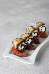 Canapes with tomato and eggplant rolls with garlic and cream cheese on white plate on gray background