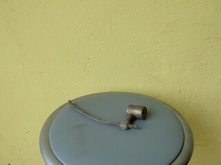 Metal cable with clamp lying on round grey stool against yellow wall.