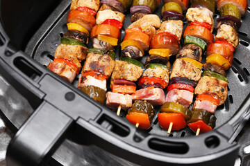 Mixed meat skewers in air fryer basket. Chicken and pork kebabs with bell pepper onion and zucchini. Hot roasted шашлык style sticks. Modern home cooking closeup. Healthy fast airfryer meal.