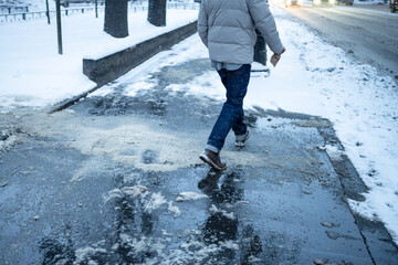 Man walks around spot with scattered technical salt and mixture of wet snow on asphalt sidewalk,...