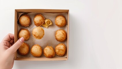 A hand presenting a box of golden-brown, bite-sized, round, baked pastries on a white surface